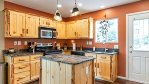 Cocina con armarios de madera, encimeras de granito, una isla central e iluminación colgante.