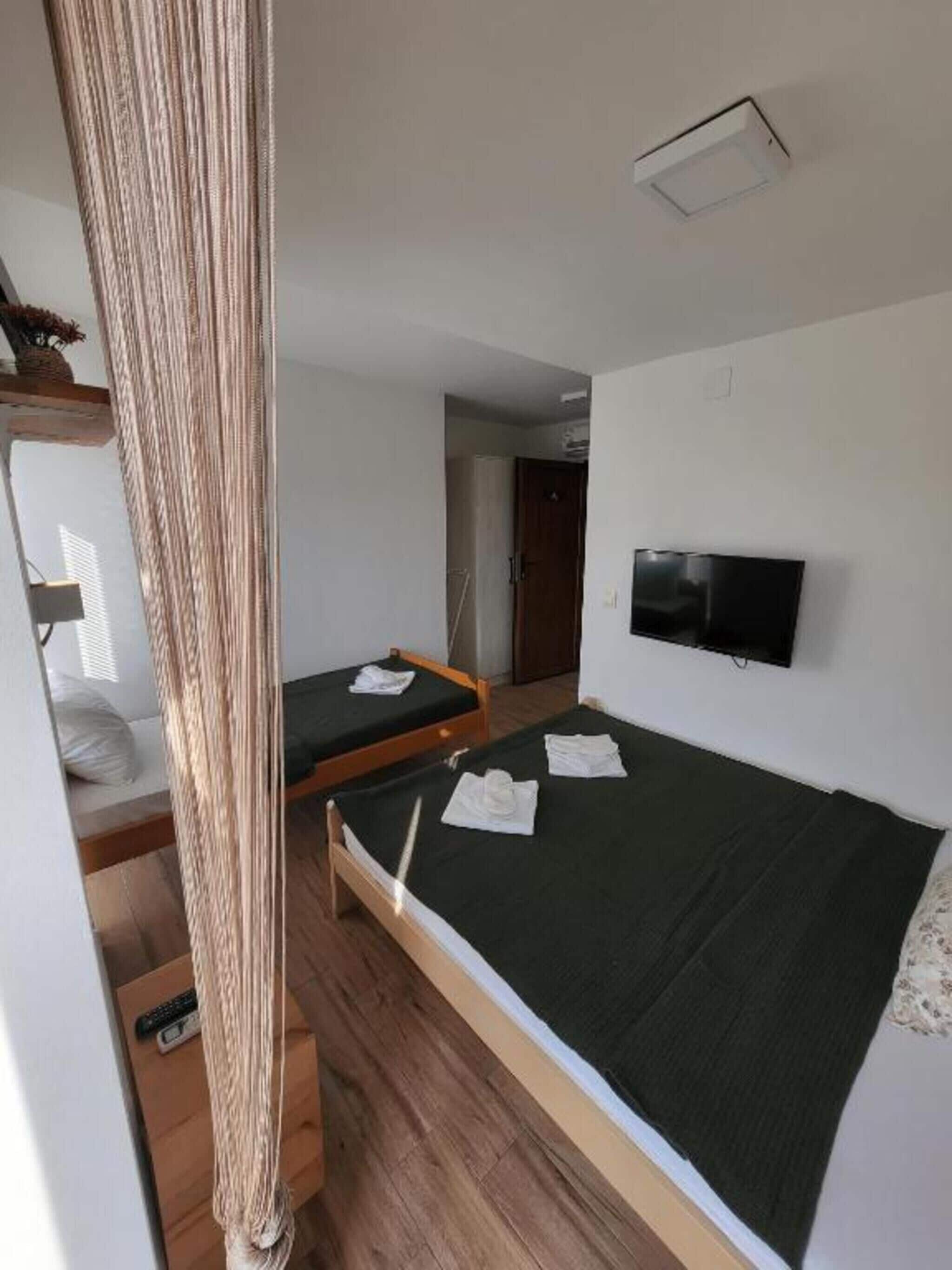 Una habitación con una cama litera, una cama individual, un televisor y una cortina.