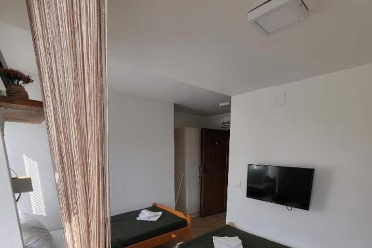 A room with a bunk bed, a single bed, a television, and a curtain.