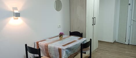 A dining area with a table, chairs, a wall-mounted light, a mirror, and a wardrobe.