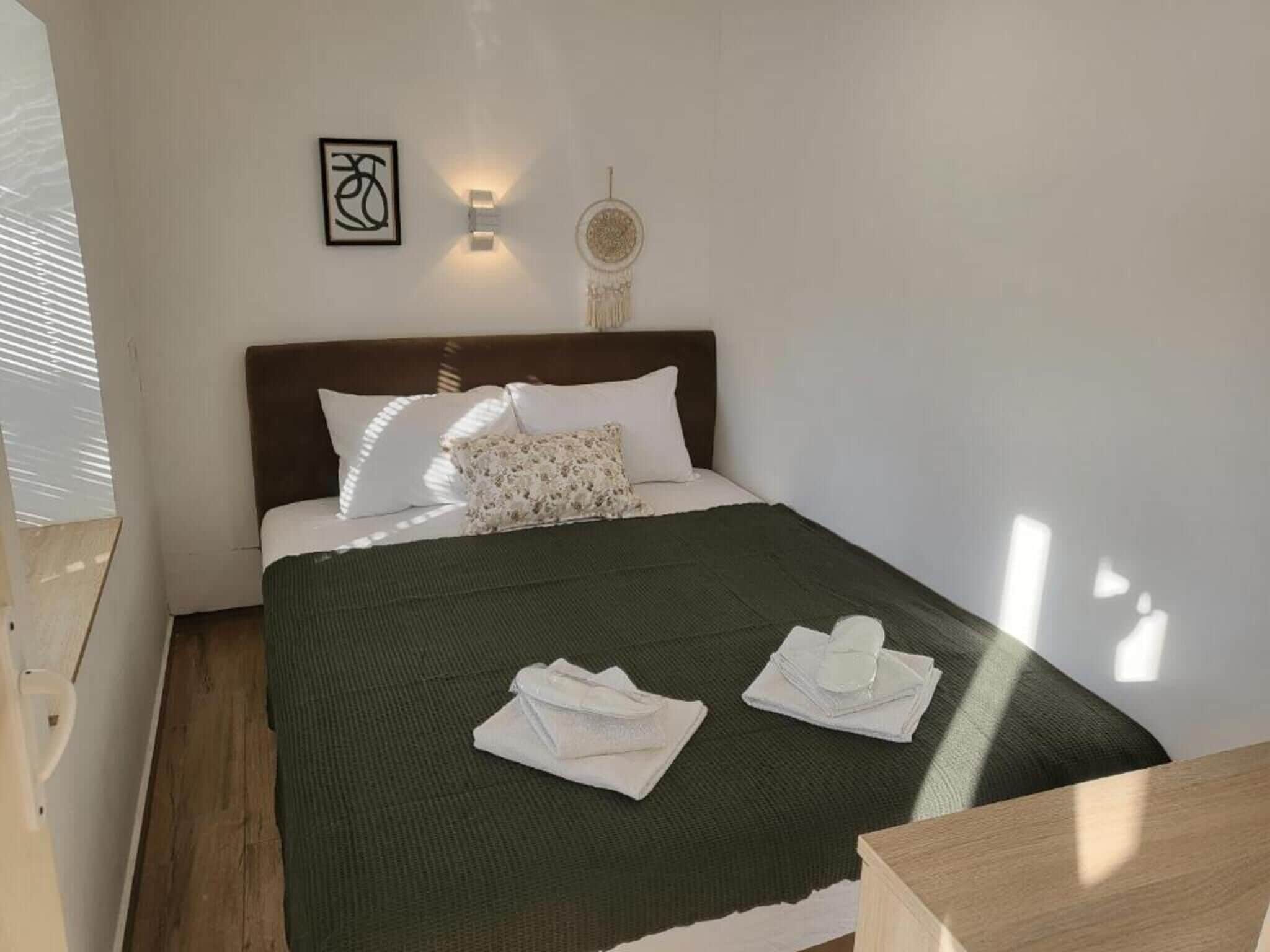 Una cama bien hecha con un edredón verde oscuro, almohadas blancas y un cabecero. Hay dos toallas blancas dobladas sobre la cama.