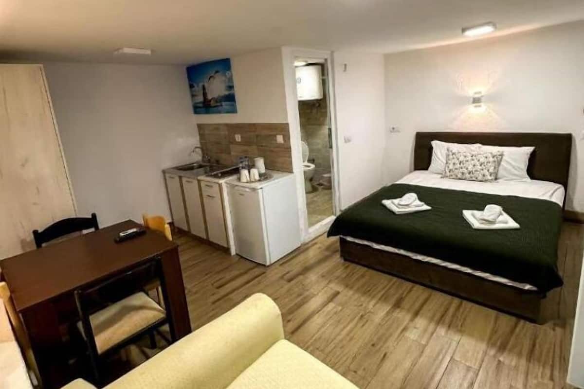 A compact hotel room with a bed, a small kitchenette, a dining area, and a bathroom.