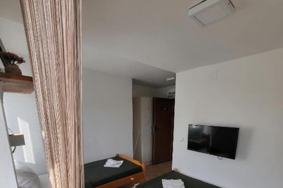 A room with a bunk bed, a single bed, a television, and a curtain.
