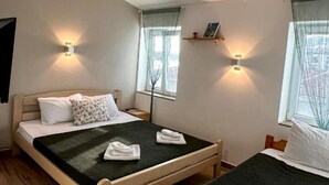 A hotel room with two beds, a wooden floor, and two windows with curtains. - SERENİTA STONE HOUSE (Rafajlovici)