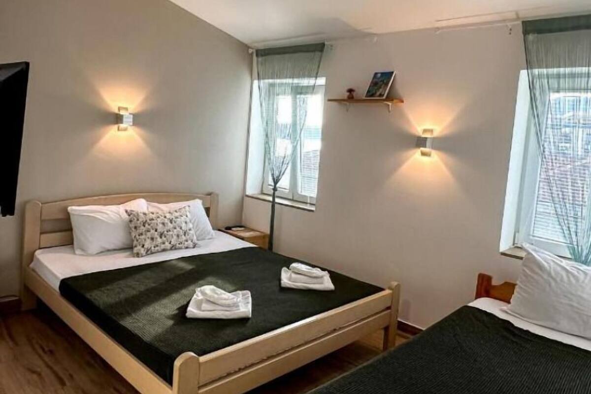 A hotel room with two beds, a wooden floor, and two windows with curtains.