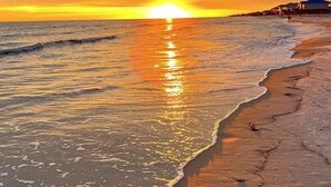 Ein Strand bei Sonnenuntergang, mit Wellen und einer fernen Küstenlinie mit Gebäuden.