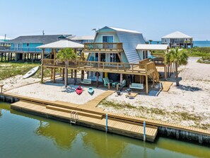 A beachfront property with a wooden deck, kayaks, and a pool. - Waterfront Beach Cottage (Dauphin Island)