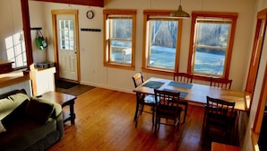 A dining area with a wooden table and chairs, a green bag hanging on the wall, and a clock on the wall. - Peaceful private location, cottage @Acadia NP, Lighthouse, Beaches, Seafood🦞 (Bass Harbor)