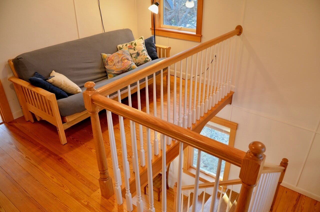 A wooden staircase with a white balustrade leading to a second floor. A grey sofa with patterned cushions is positioned on the first floor.