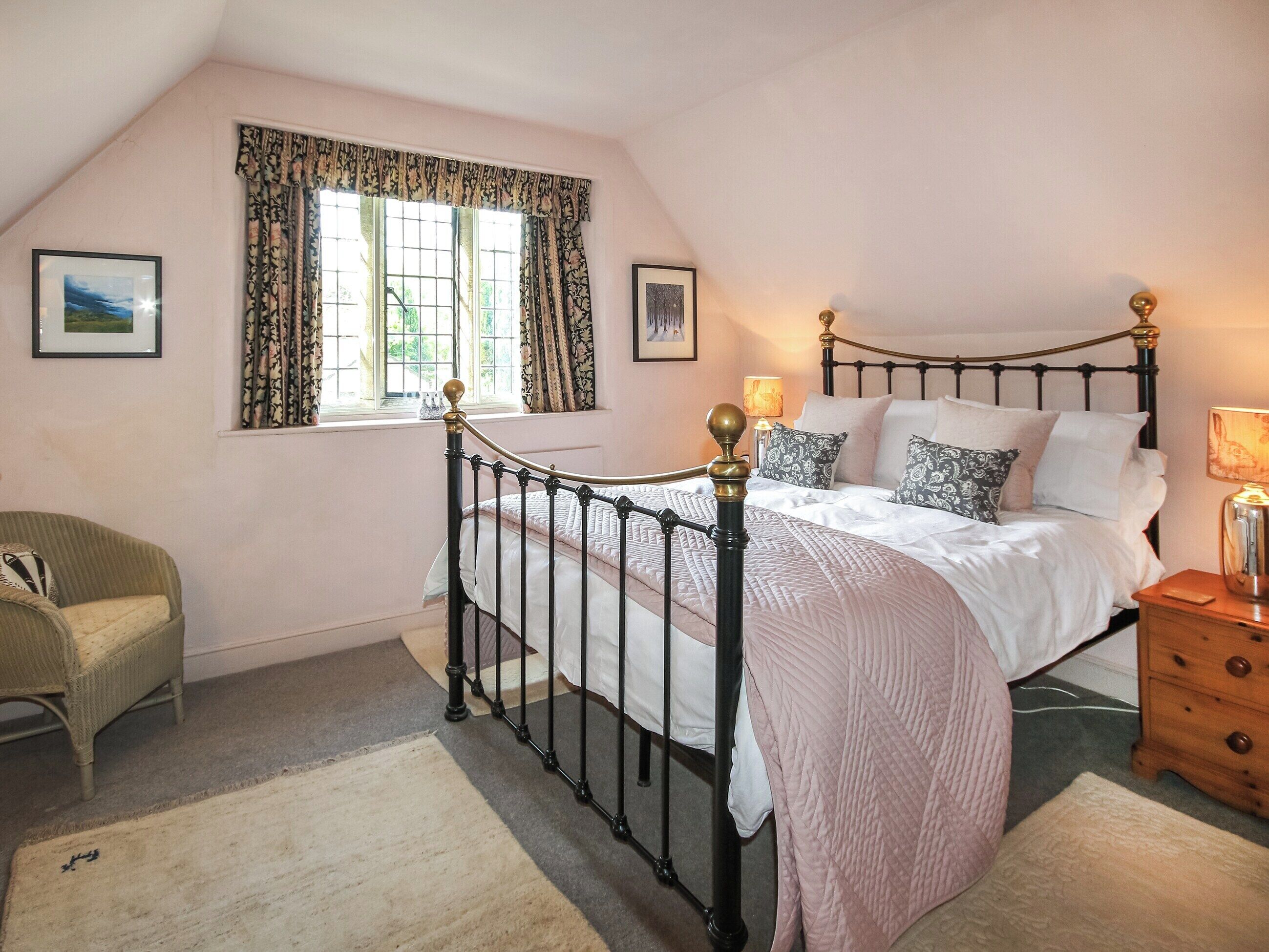 A bedroom with a bed, a nightstand, a chair, a window with curtains, and a picture on the wall.
