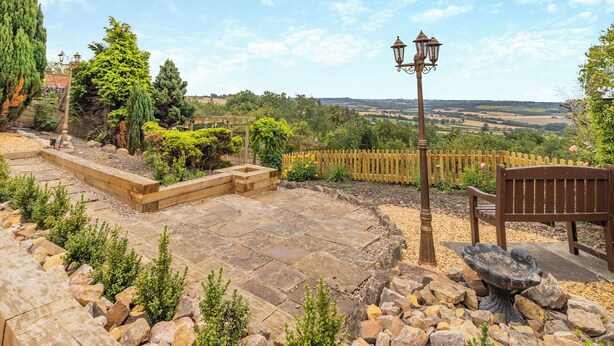 A garden patio with stone flooring, a wooden bench, a bird bath, and a wooden fence. - 5 bedroom accommodation in Chesterfield (Chesterfield)