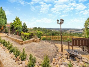 A garden patio with stone flooring, a wooden bench, a bird bath, and a wooden fence. - 5 bedroom accommodation in Chesterfield (Chesterfield)