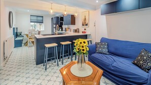 A modern living room with a blue sofa, a wooden coffee table with a vase of sunflowers, and a kitchen area in the background. - 5 bedroom accommodation in Chesterfield (Chesterfield)