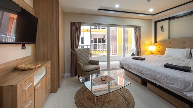 A modern hotel room with a bed, a flat-screen TV, a glass coffee table, a chair, and a balcony with a view. - New Nordic Trend 2 by Apartwell (Pattaya)