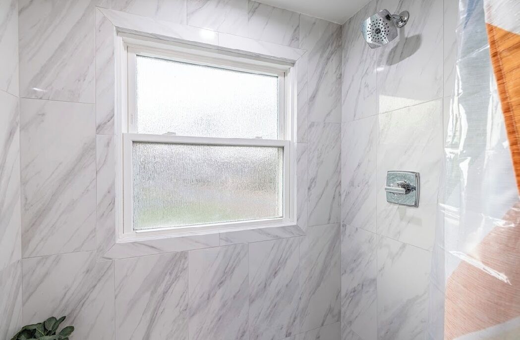 A bathroom with marble walls, a window, a shower, and a towel rack.