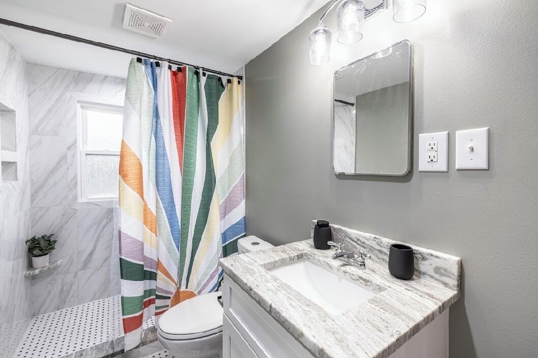 A bathroom with a striped shower curtain, a marble sink, a mirror, and a potted plant.