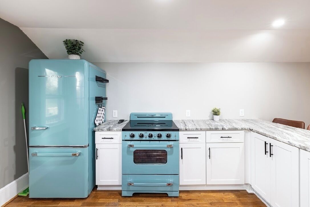 A kitchen with a blue refrigerator, a stove, and white cabinets.