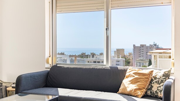 Un salon avec un canapé, une table basse en verre et une vue sur la mer et les bâtiments.