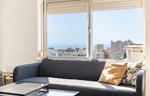 Un salon avec un canapé, une table basse en verre et une vue sur la mer et les bâtiments.