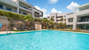 A modern swimming pool with clear blue water, surrounded by a multi-story building with balconies and outdoor seating areas. - Cozy apartment in Estepona (Estepona)