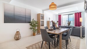 A modern dining area with a wooden table, grey chairs, a hanging light fixture, and a large window with red curtains. - Cozy apartment in Estepona (Estepona)