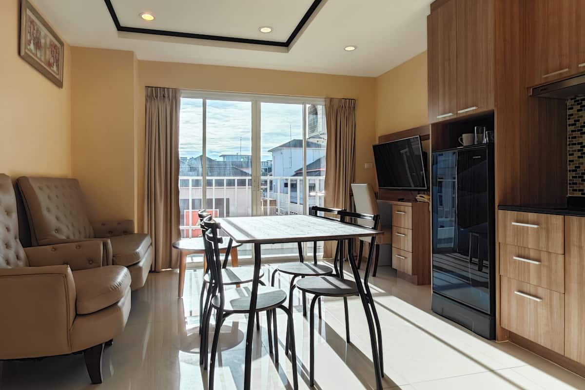 A modern kitchen with a dining table and chairs, a sofa, and a large window with a view of buildings.
