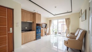 A modern kitchen with wooden cabinets, a built-in oven, and a dining area with a glass table and beige sofa. - New Nordic Trend 5 by Apartwell (Pattaya)