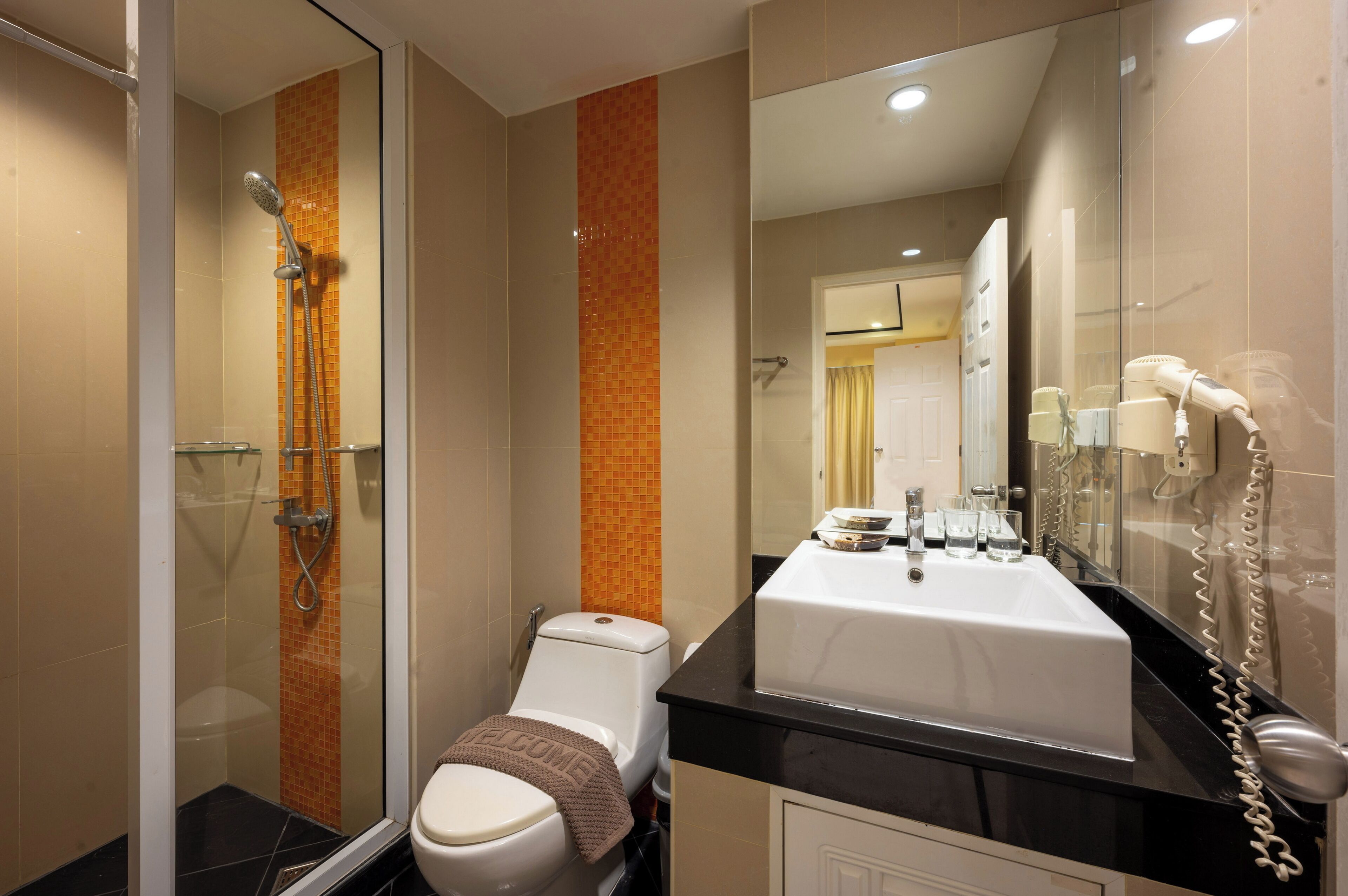 A modern bathroom with a glass-enclosed shower, a white toilet, a black countertop with a sink, and a mirror.