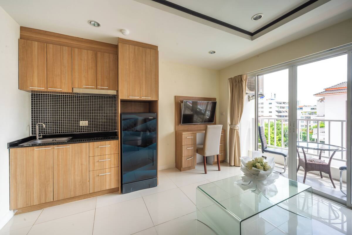 A modern kitchen with wooden cabinets, a black refrigerator, and a glass dining table.