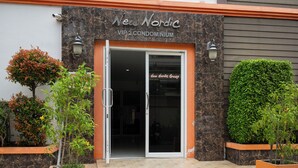 L’extérieur du New Nordic VIP 2 Condominium, avec son entrée en verre, ses plantes en pot et une enseigne indiquant le New Nordic Group.