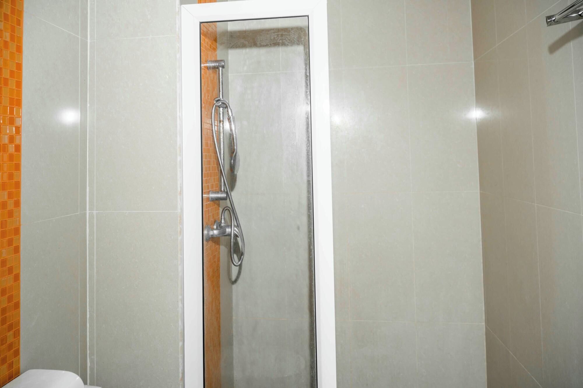 Ducha con puerta de cristal, paredes de azulejos y cabezal visible.