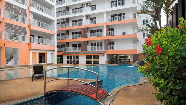 Un hôtel à plusieurs étages doté d’une piscine, de balcons et d’un palmier.