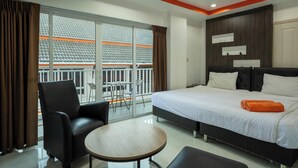 Une chambre d’hôtel moderne avec un grand lit, une petite table ronde et un balcon offrant une vue sur la façade de l’immeuble.