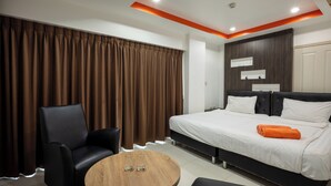 Une chambre d’hôtel moderne avec un grand lit, une table ronde en bois, un fauteuil en cuir noir et des rideaux marron.
