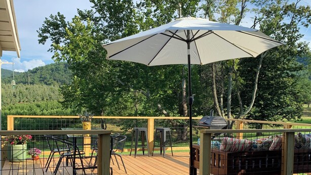 Une terrasse en bois avec des meubles d’extérieur, un barbecue et un grand parasol.
