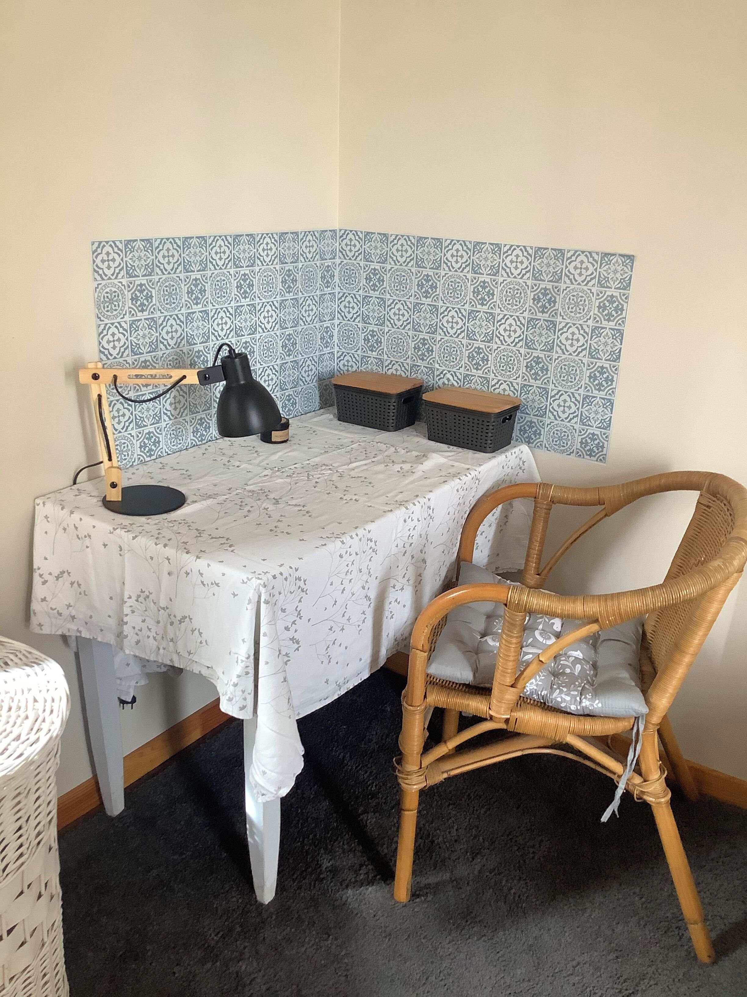 Et lille, pænt indrettet arbejdsområde med skrivebord, stol, lampe og opbevaringskurve.