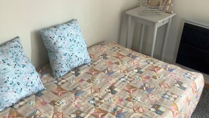 Un dormitorio con una cama, dos almohadones estampados, una mesita de noche y una televisión.