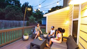 Un patio con mobiliario exterior, plantas en macetas y luces colgantes.