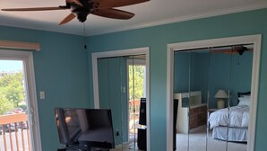 A bedroom with a bed, a TV, a ceiling fan, and a sliding door leading to a balcony. - nestled against the dunes, south end beach block on cul-de-sac (Brigantine)