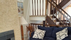 A living room with a dark blue sofa, patterned cushions, a fireplace, and a wooden staircase. - nestled against the dunes, south end beach block on cul-de-sac (Brigantine)