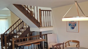 A dining area with a wooden table and chairs, a staircase with wooden railings, and a ceiling light fixture. - nestled against the dunes, south end beach block on cul-de-sac (Brigantine)