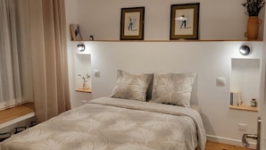 A bedroom with a bed, a hanging light fixture, a shelf with books, and a small plant. - Charme Breton à 20 min de Saint-malo - 2 Chambres à 500 m du Golf du Tronchet (Le Tronchet)