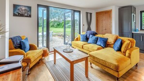 Un salon spacieux avec un ensemble de canapés jaunes, une table basse en bois et une grande porte-fenêtre coulissante donnant sur un jardin.