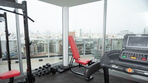 A gym with a treadmill, weight bench, and dumbbells, with a city view through large windows. - Palermo Cultura Arte y Entretenimiento (Buenos Aires)