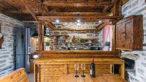 Una cocina rústica con vigas de madera, una pared de piedra y un mostrador de madera con copas de vino y una botella.