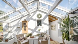 A sunlit room with a high ceiling, a wooden cabinet, a table with chairs, and potted plants. - 3 bedroom beautiful home in Kalundborg (Kalundborg)