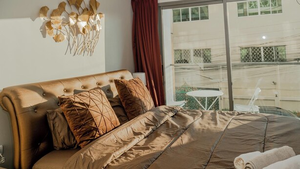 A bedroom with a large bed, a decorative wall piece, and a view of the outside.
