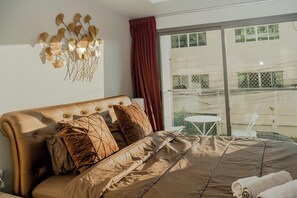 A bedroom with a large bed, a decorative wall piece, and a view of the outside.