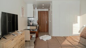 A hotel room with a bed, a TV on a wooden dresser, a desk with a chair, and a kitchenette.