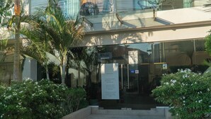A modern building entrance with glass doors, a signboard, and surrounding greenery.